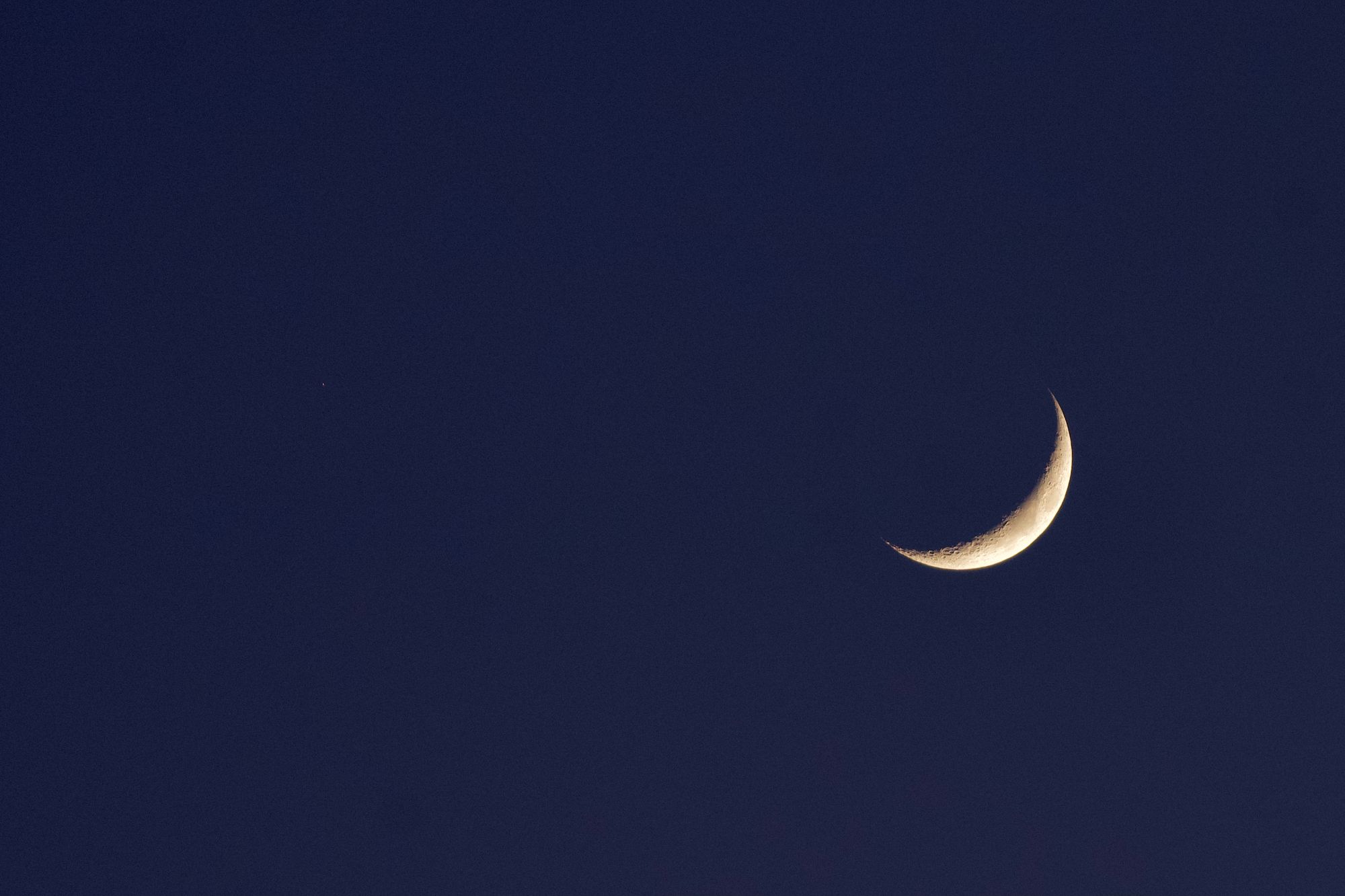 A photo of the waxing crescent moon seen against a dark blue sky near moonset.